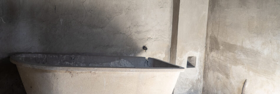 A concrete bathtub, tilted on a concrete slab, is shown against concrete walls.